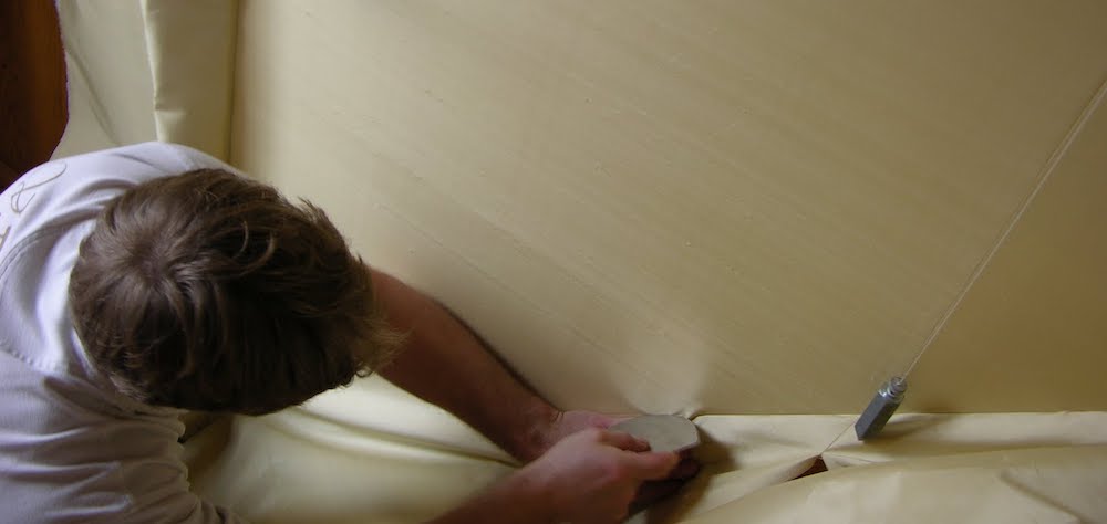 tapissier qui rentre un tissu uni jaune sur le mural